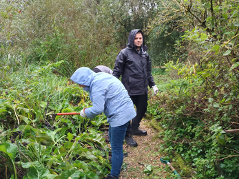 Tansy and Lewis in rain jackets cutting vegetation around a path