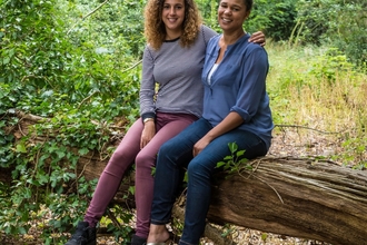 Juliet and Amy sit together on a fallen tree