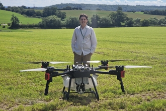 A man stands behind a very large drone in a field