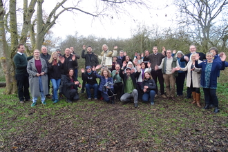 Large group posing for photo outside under bare trees, waving to camera