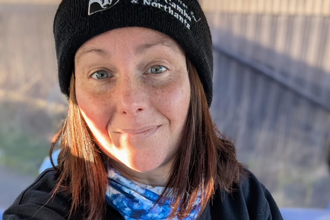 Jasmin takes a selfie wearing a black Wildlife Trust logo beanie hat and logo sweatshirt