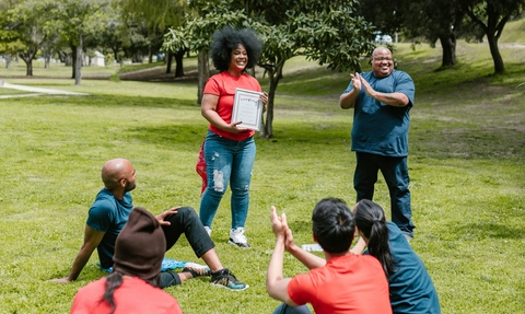 A woman is applauded as she stands in a grassy park holding award