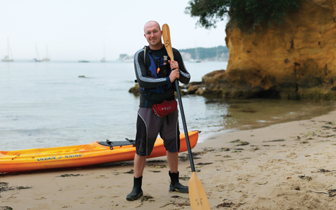 Dan stands on a beach with his kayak