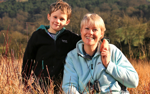 Kati and her son sat in a field with woods in background