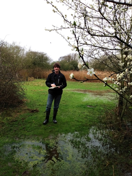 Nathanael stands in a partially flooded grass meadow with tree surrounding