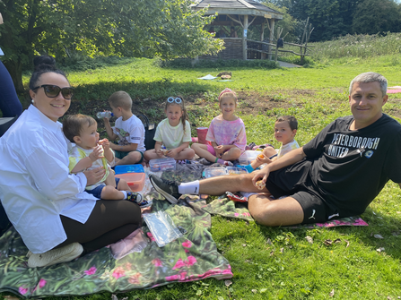 Mum and dad picnic with five young children in a sunny nature reserve