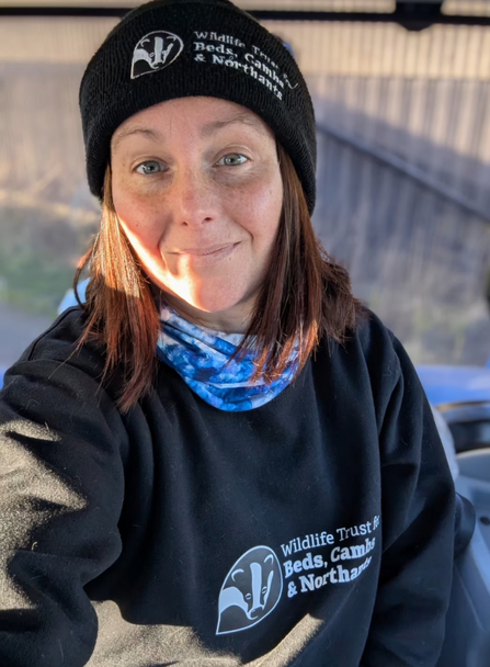 Jasmin takes a selfie wearing a black Wildlife Trust logo beanie hat and logo sweatshirt