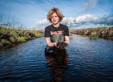 Filip stands in the water holding mud