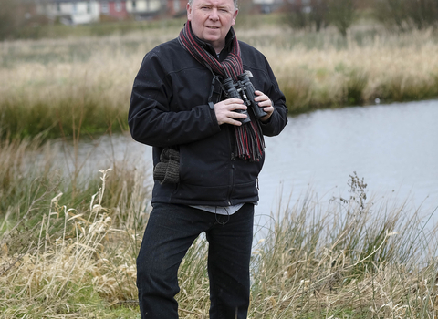 Aidan stands with his binoculars on a reserve