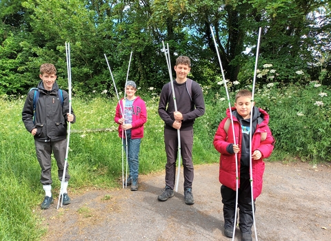 Four young people stand holding white poles in front of long grass and trees