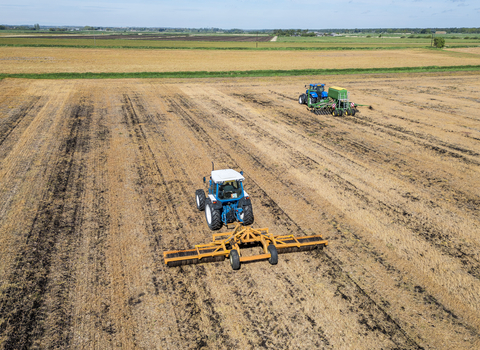 Two tractors ploughing and seeding a farm, taken from a drone